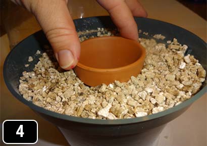 A clay flowerpot with a sealed hole being twisted into vermiculite in a larger, plastic pot.